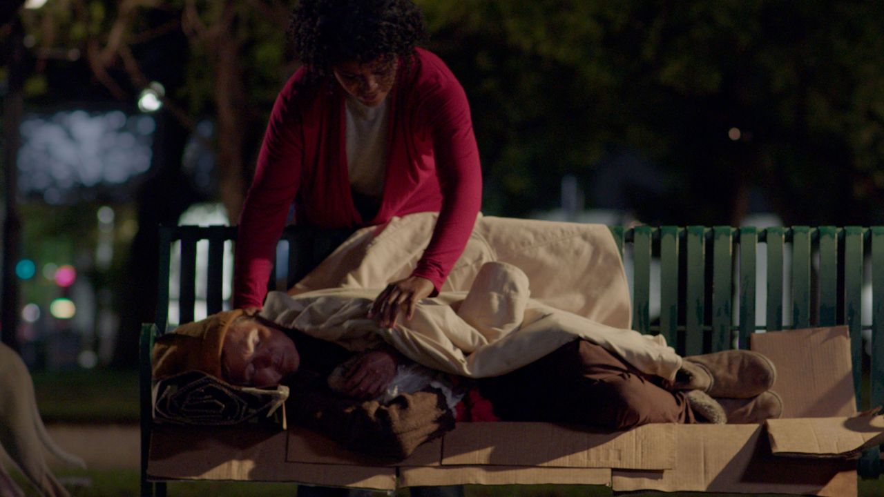 A woman covering a homeless man with her coat